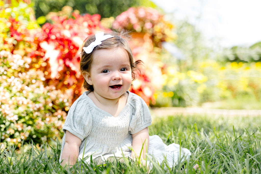 A baby girl sitting in a flower garden, smiling