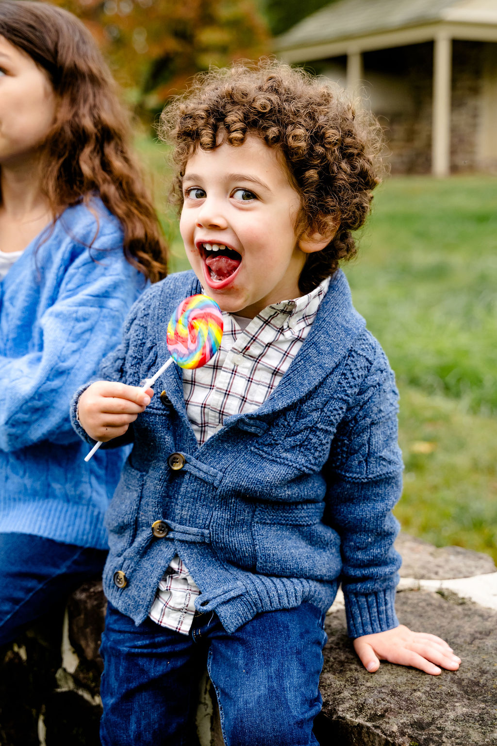 A curly-haired boy pulling a silly face with a lollipop