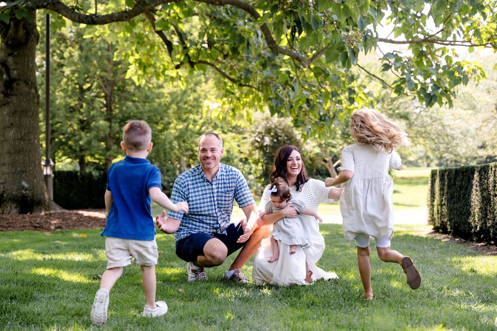 A family laughing and chasing each other across a sunny lawn