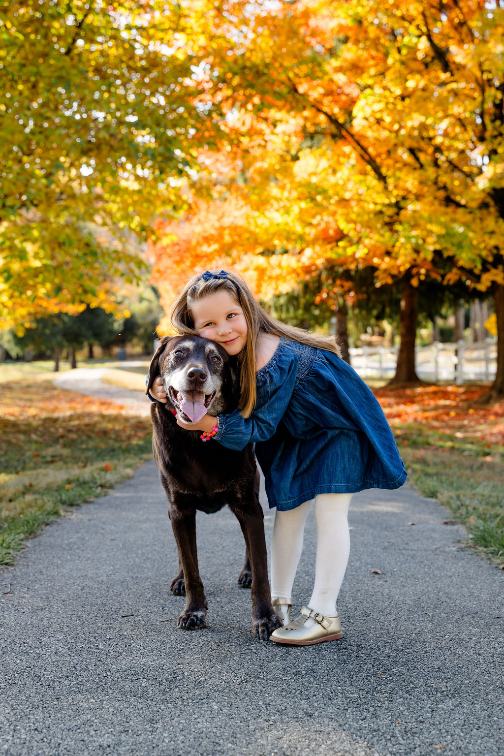 A girl hugging her dog on a leafy path
