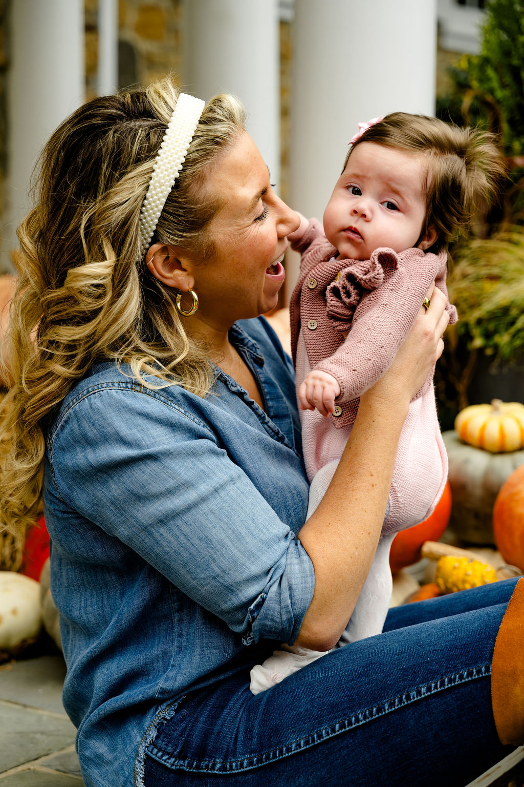A mom lifting her baby among pumpkins on the porch
