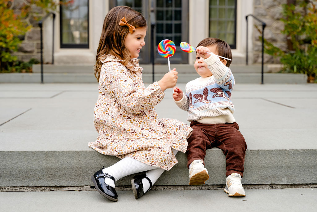 A sister offering her little brother a lollipop on stone steps