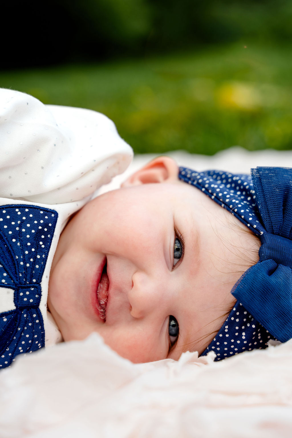 A smiling six-month-old lying on a blanket outdoors