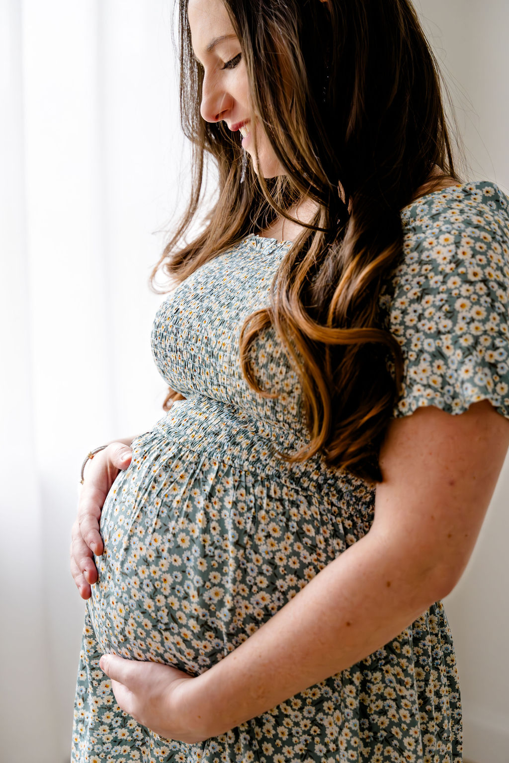 An expecting mother cradling her bump by a bright window