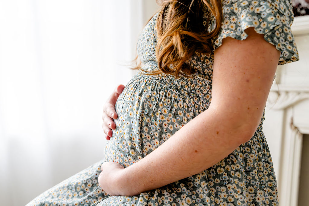 An expecting mother in a floral dress by the window