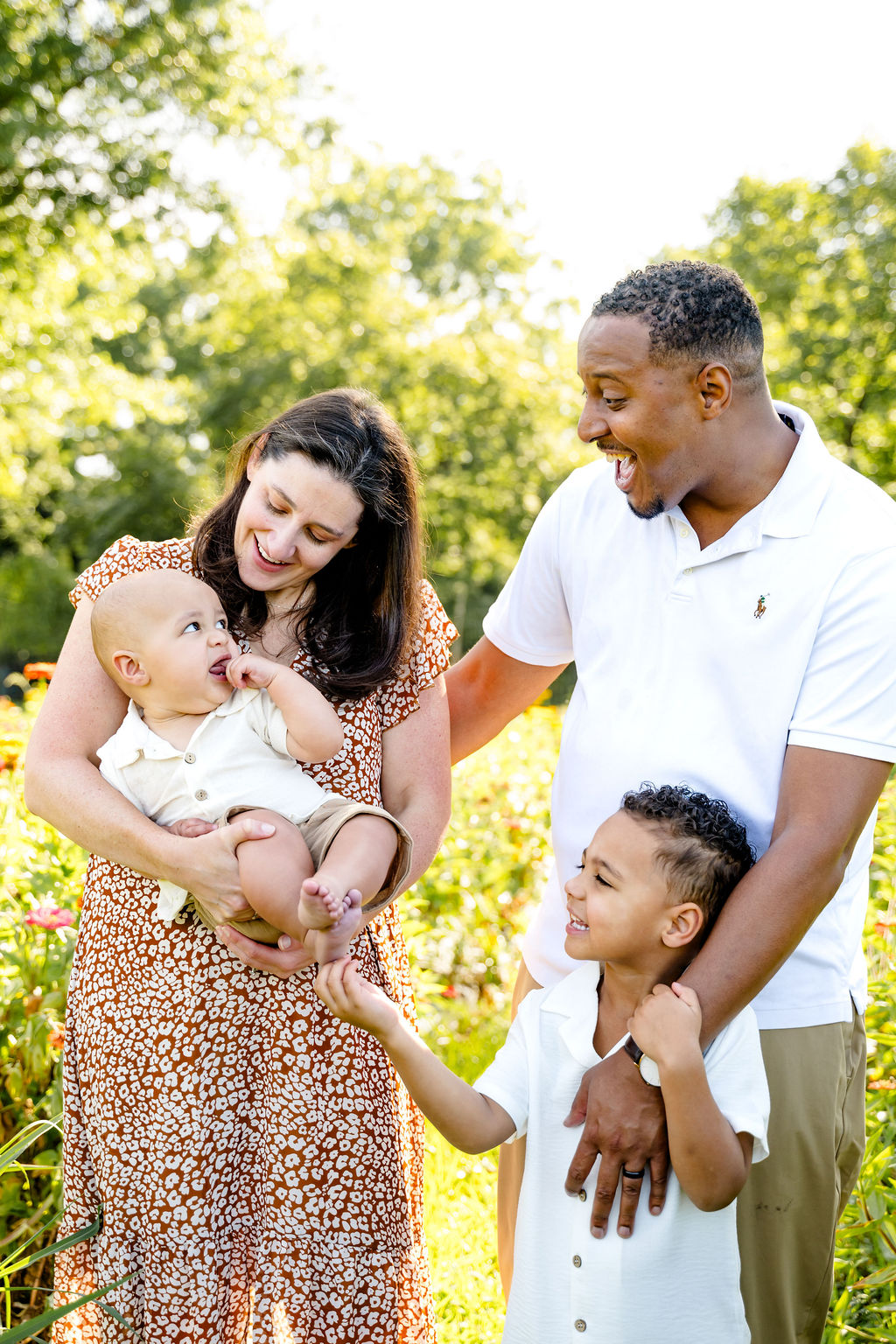 Parents laughing with their baby and young son in a flower garden